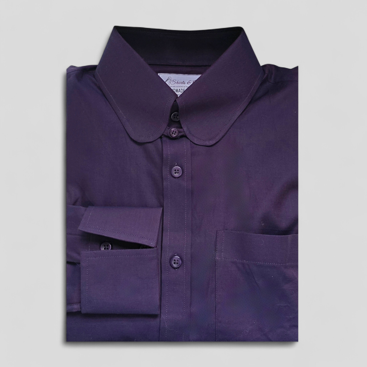 Folded dark purple two‑tone penny collar shirt with visible label and buttoned cuff.